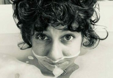 Black and white photo of Allison, writer, in bubble bath with half her face underwater & curly hair