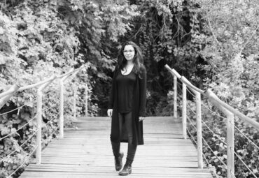 Rae, Content Manager, black and white photo of her standing on a bridge with trees on either side